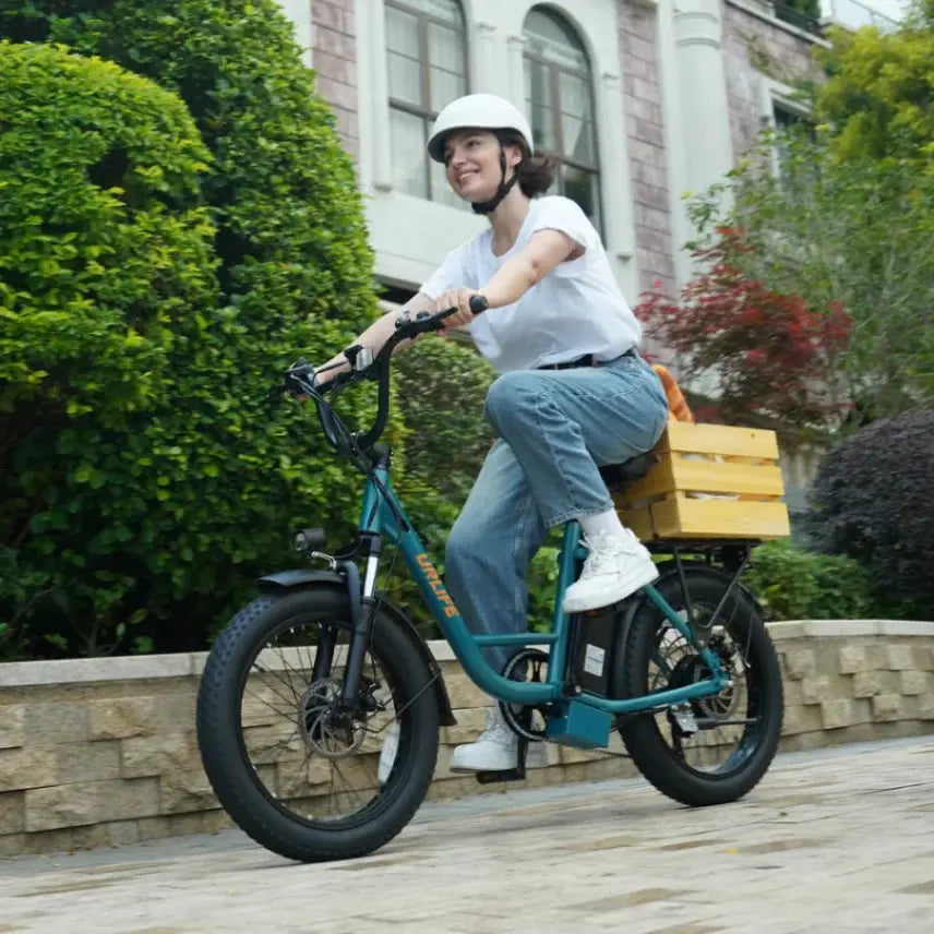 Woman riding a green URLIFE E20 electric bike with a wooden crate on a sidewalk.