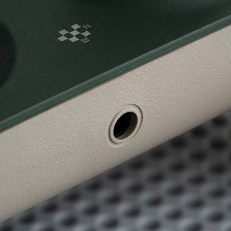 Close‑up of a green and beige gaming controller edge showing a 3.5 mm audio jack port and a small pixel‑style logo, highlighting the textured matte finish and refined material contrast.
