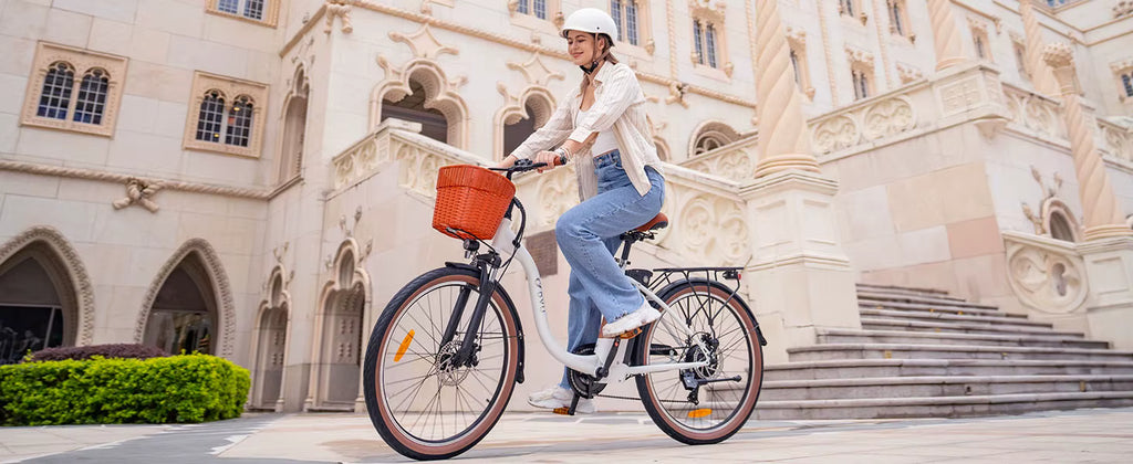 Woman riding a White DYU C6 Pro E-Bike electric bicycle with an orange basket in front of a historic building