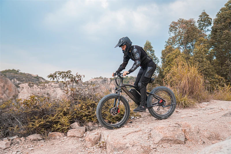 Rider wearing protective gear riding a LANKELEISI MG740PLUS full suspension fat tyre electric mountain bike through a forest trail with autumn leaves and trees.
