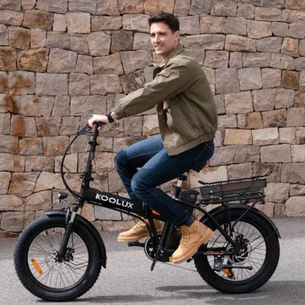 Man riding a KOOLUX X11S electric bike against a stone wall.
