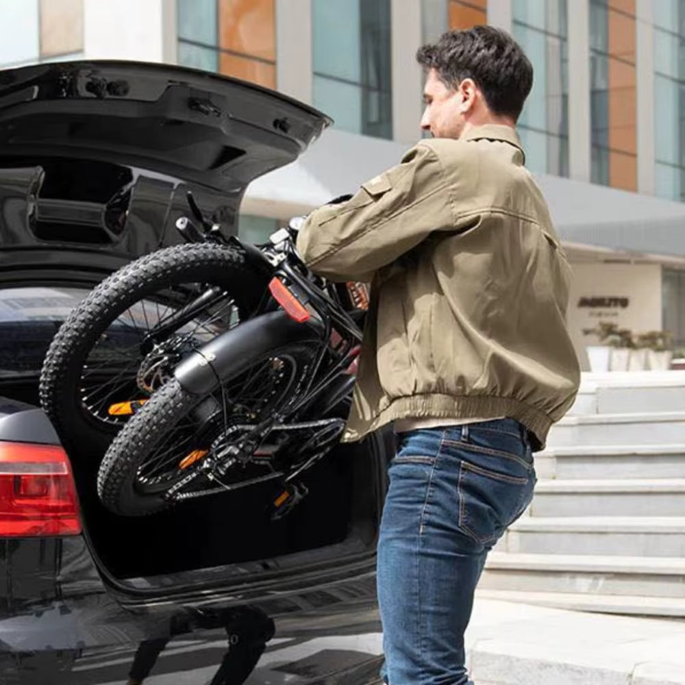 Man loading a KOOLUX X11S folded electric bicycle onto a car trunk in an urban setting.