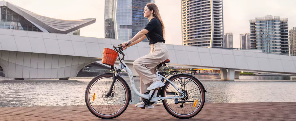 Person riding a White DYU C6 Pro E-Bike electric bicycle with a basket in an urban setting with modern buildings and water.