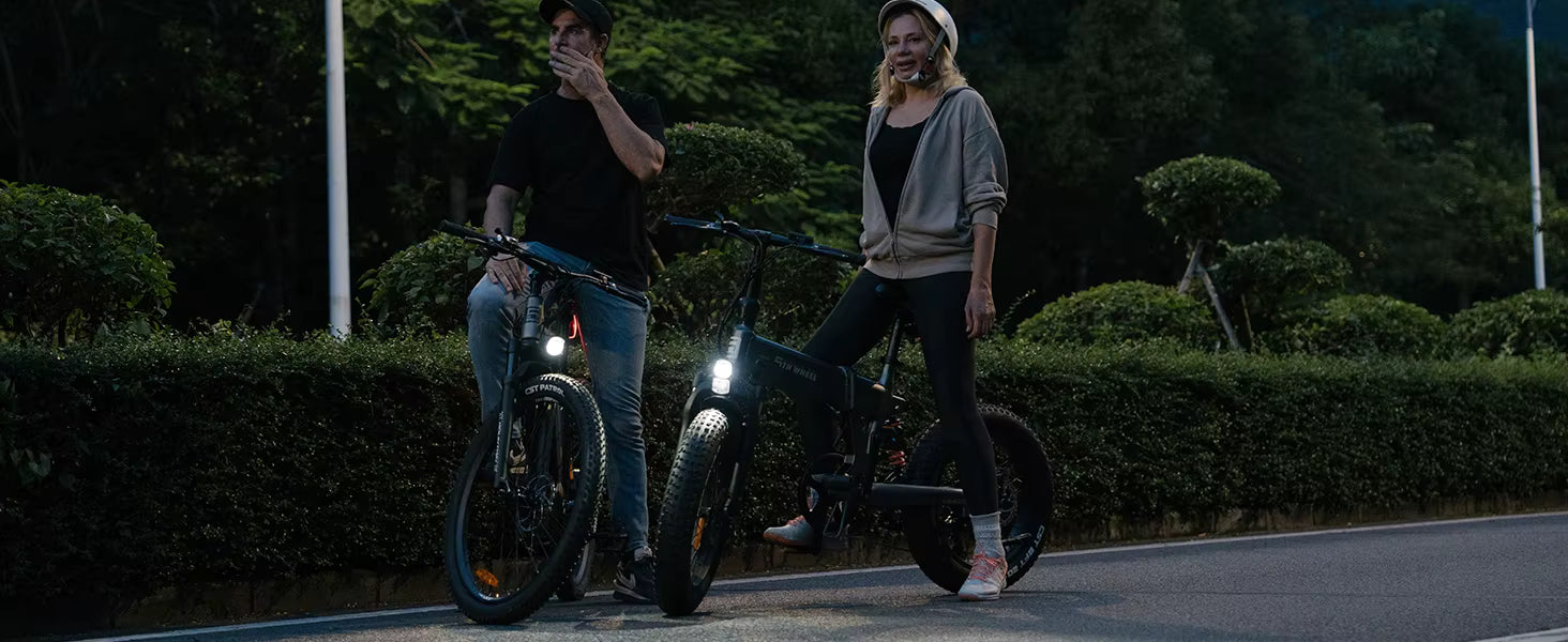 Two people with electric bikes on a dark road with trees in the background