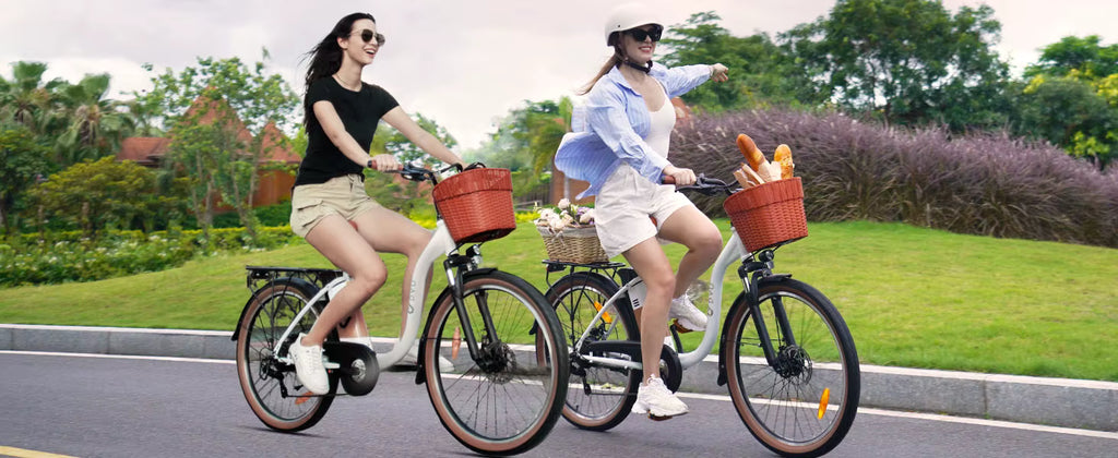Two women riding White DYU C6 Pro E-Bike electric bicycles with baskets on a road surrounded by greenery