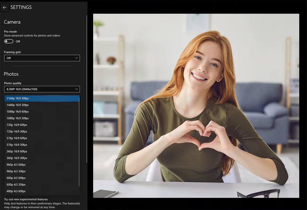 Woman making a heart shape with her hands in a room with a camera settings interface on the left.