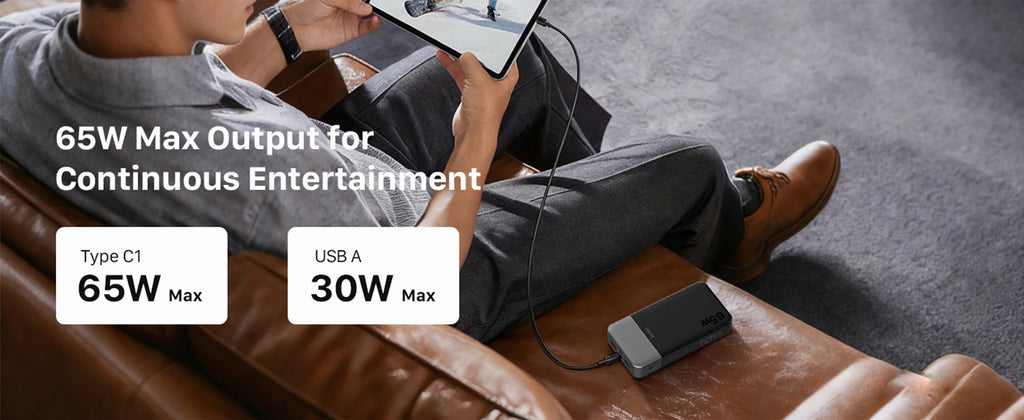 A man reclining on a brown leather couch while charging a tablet and phone with a portable power bank. Text overlays highlight 65W max output and 30W max USB-A output.