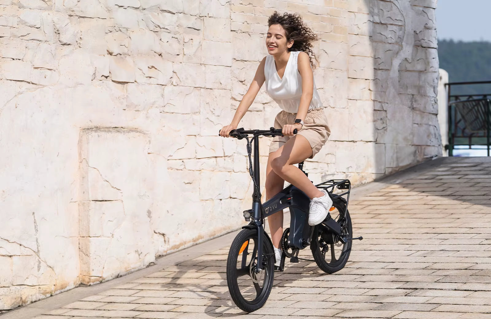 Woman riding a black electric bike against a stone wall.