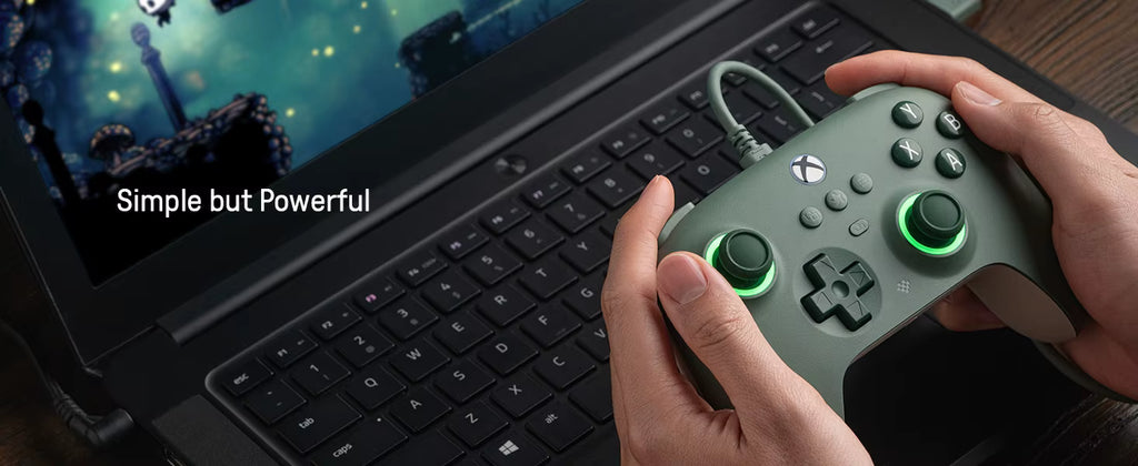 Person holding a green gaming controller in front of a laptop displaying a game.