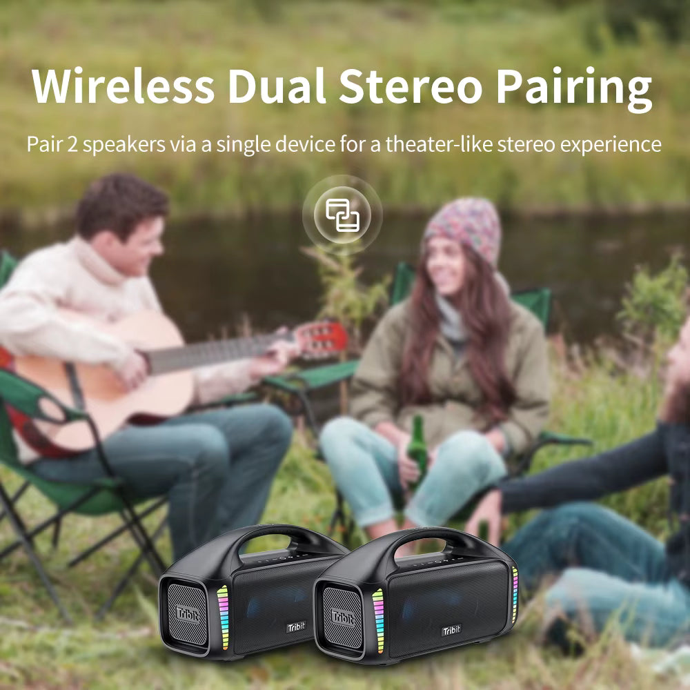 Two Tribit StormBox Blast speakers placed outdoors on the grass in front of people camping, demonstrating wireless dual stereo pairing.