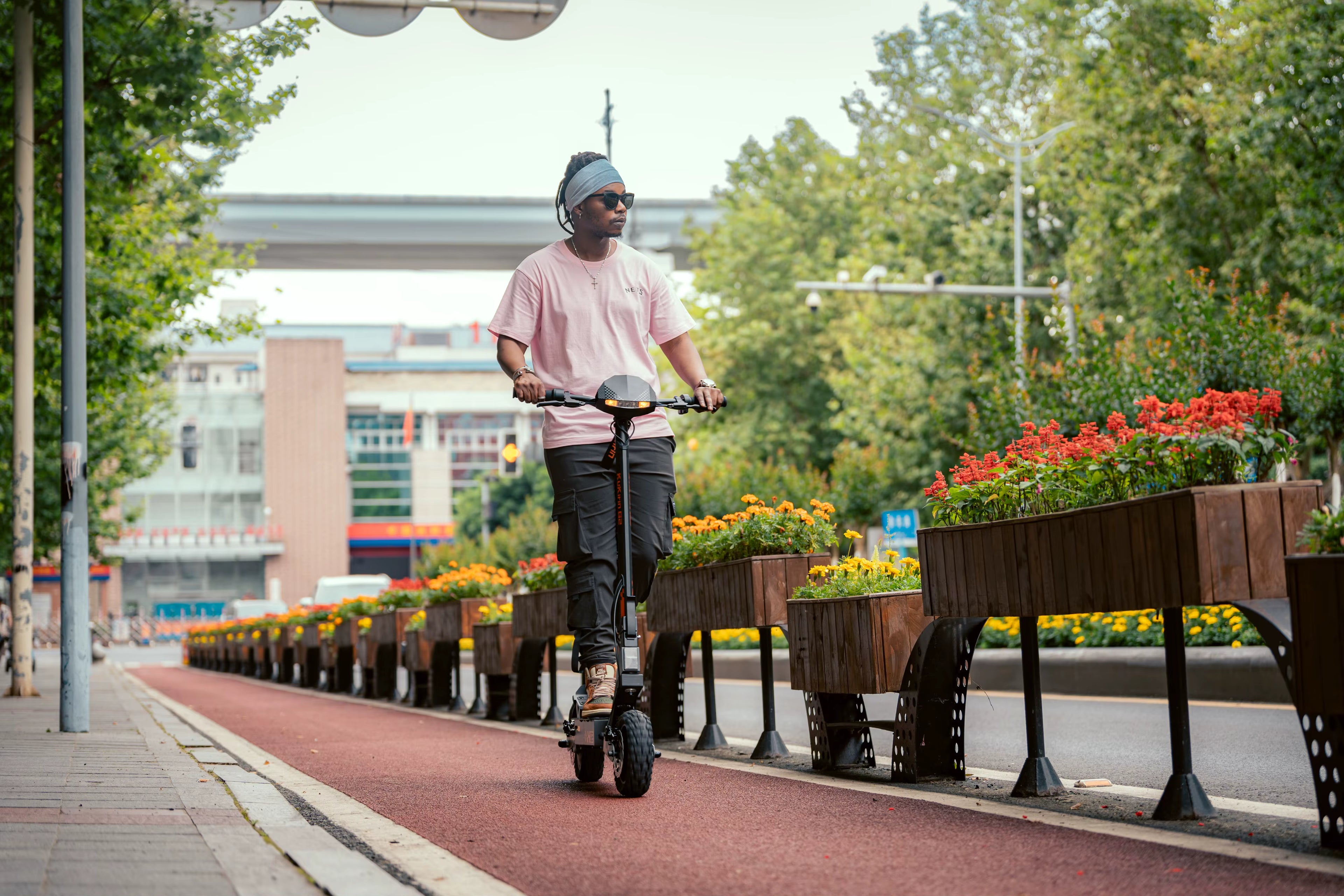 Person riding an electric scooter on a sidewalk with decorative planters and trees in the background