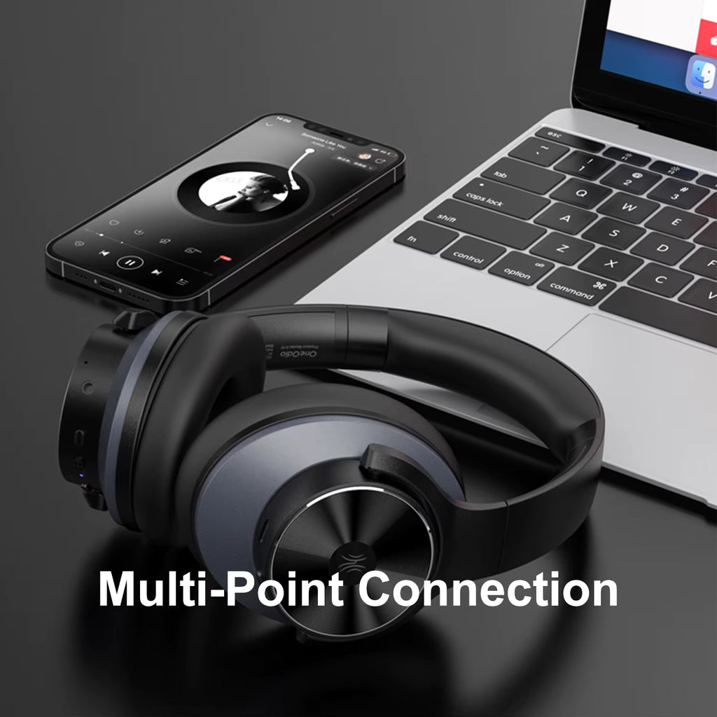 OneOdio A10 Hybrid ANC Over-Ear Bluetooth Headphones with smartphone and laptop on a dark surface, highlighting multi-point connection feature.