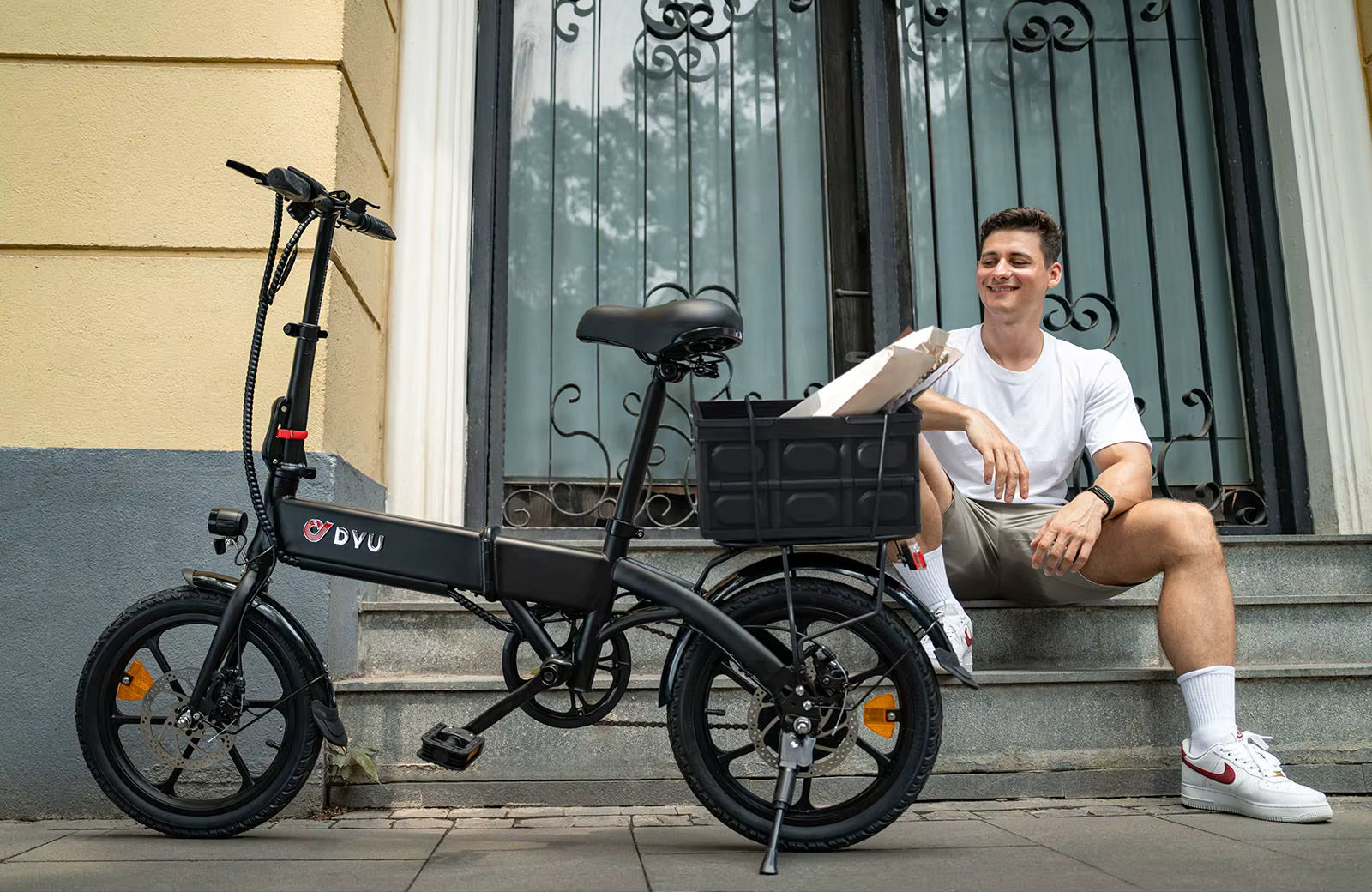 Man sitting on steps next to a black electric bike  DYU A1F Pro Folding E-Bike  with a basket.