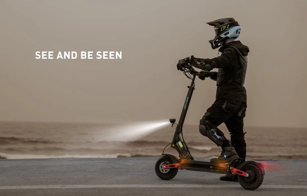 Person riding a scooter with text 'See and be seen' on a beach.