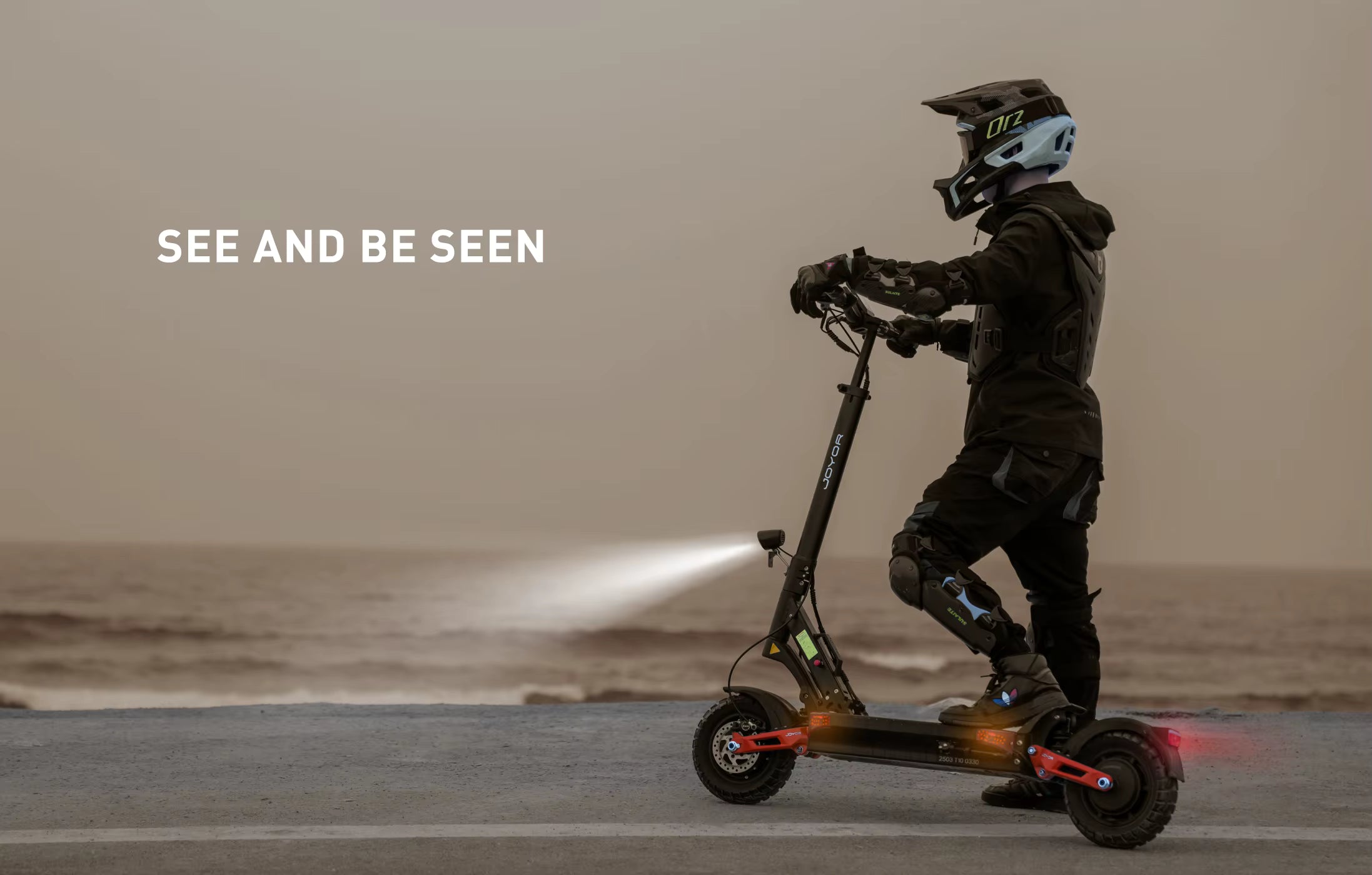 Person riding a scooter with text 'See and be seen' on a beach.
