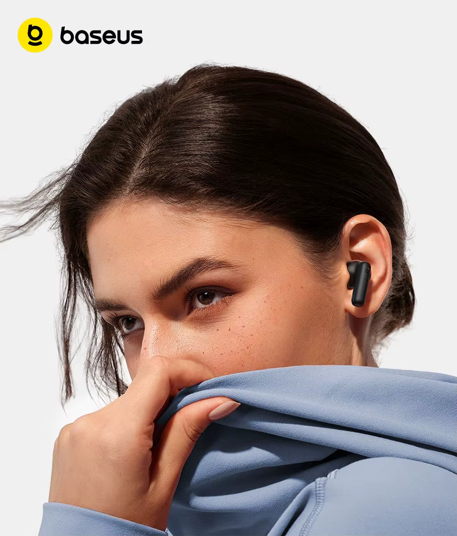 A close-up lifestyle shot of a woman wearing a black Baseus wireless earbud, looking over her shoulder while pulling up a light blue hoodie. The Baseus logo is visible in the top-left corner.