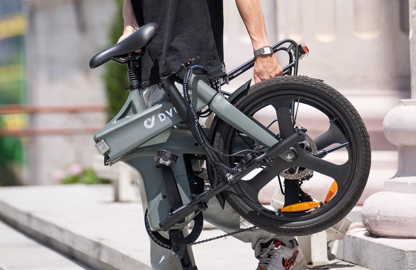 Person holding a folded electric bike with 'DVI' branding on a blurred background