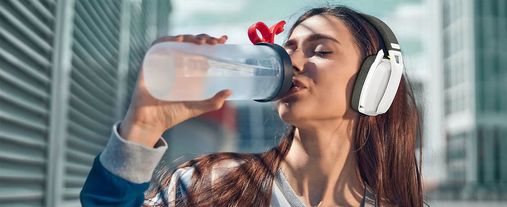 Lifestyle photograph of a person wearing the white headset while drinking water after a workout