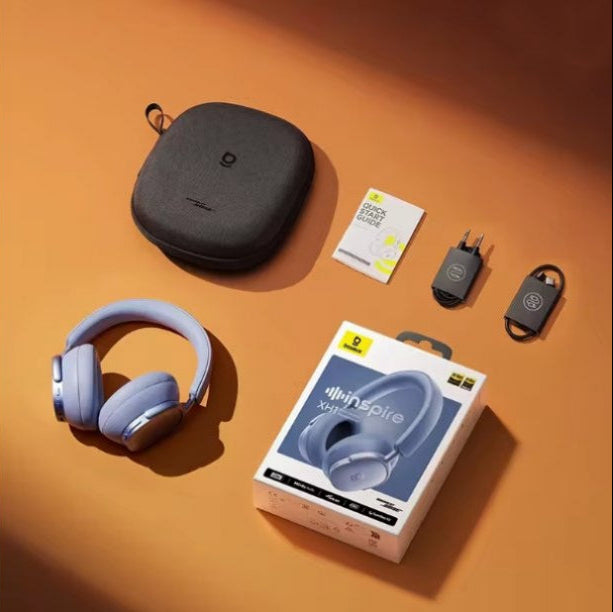 A pair of Twilight Blue over-ear Baseus Inspire XH1 headphones with a matching hard carrying case, shown with the retail box, a small card, and two small accessories on an orange surface.