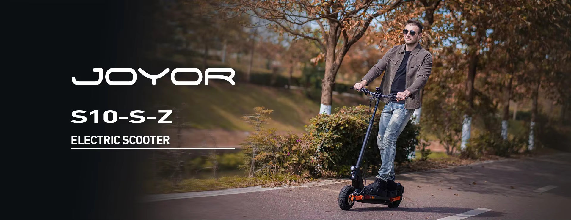 Man riding a Joyor S10-S-Z electric scooter on a path with trees and grass in the background