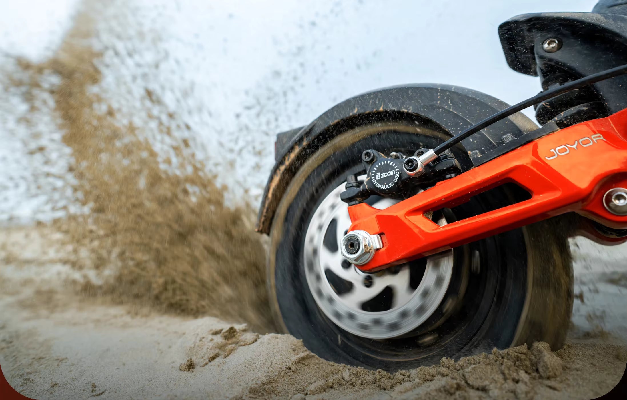 Close-up of a scooter wheel with 'Joyor' branding on a sandy beach surface.