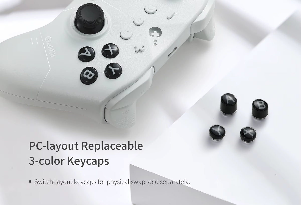 GuliKit ES Controller in white finish highlighting PC‑layout replaceable keycaps. Text reads “PC‑layout Replaceable 3‑color Keycaps – Switch‑layout keycaps for physical swap sold separately.” Controller shown with ABXY buttons and four detached black keycaps on a white surface, emphasizing customizable design for different gaming layouts.