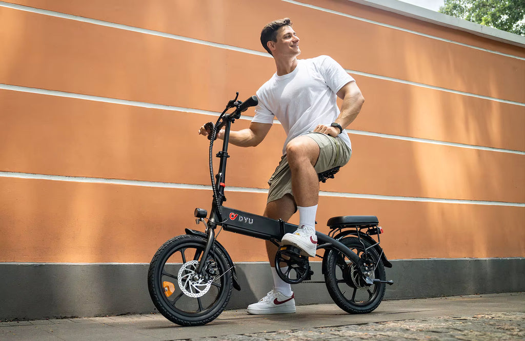 Man sitting on a black DYU A1F Pro Folding E-Bike electric bike with 'DyU' branding against an orange wall.