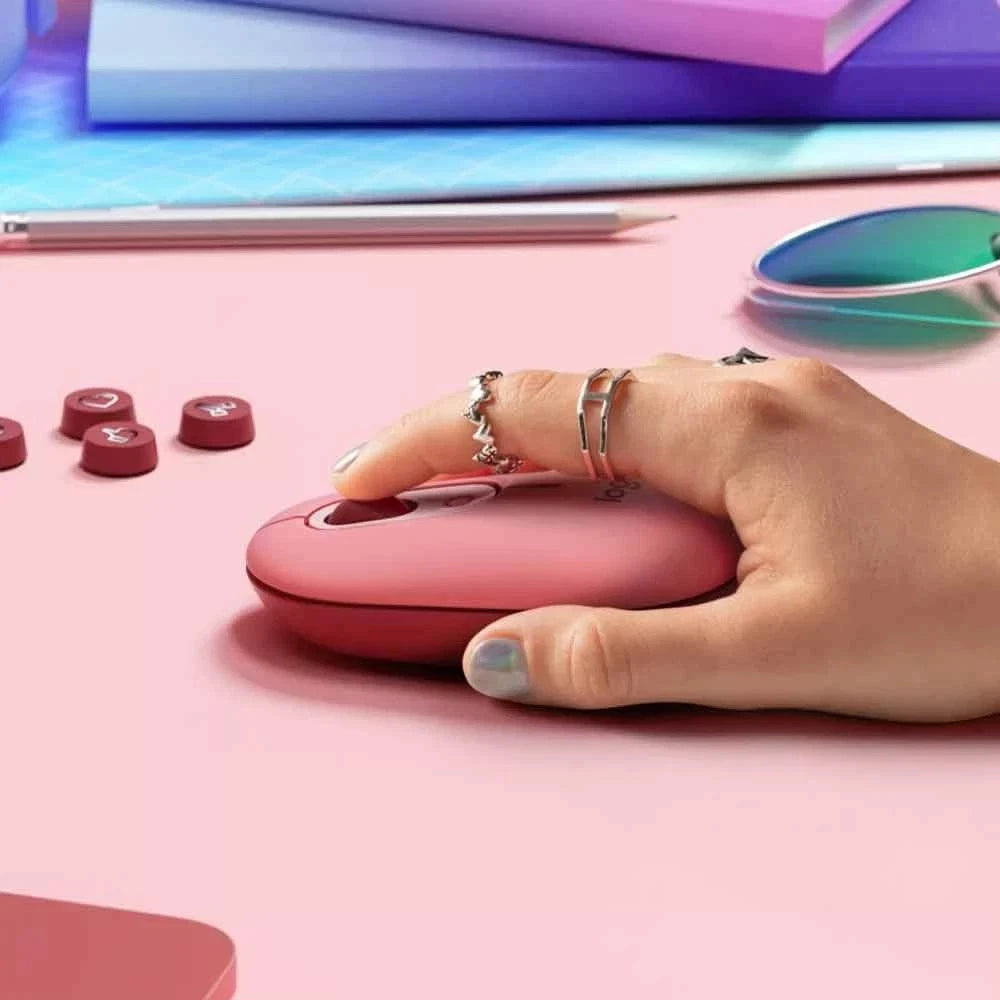 Hand using a pink computer mouse on a pink surface with colorful books in the background