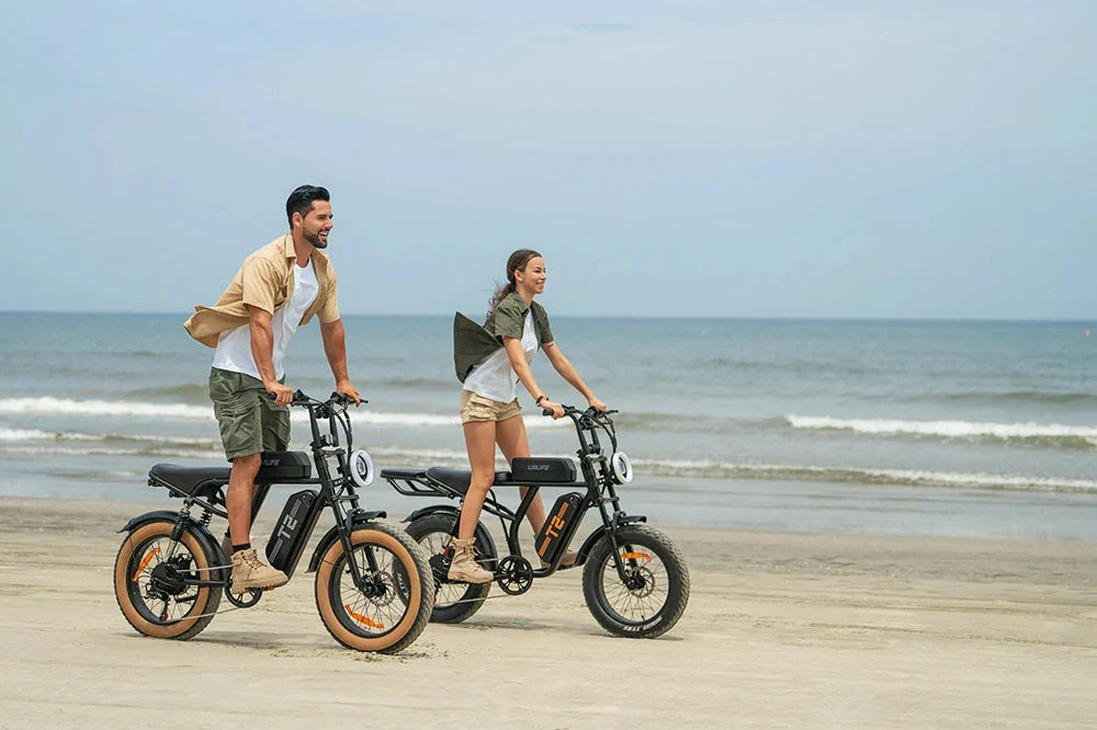 Man and woman riding URLIFE T20 fat tire electric bikes along a sandy ocean beach